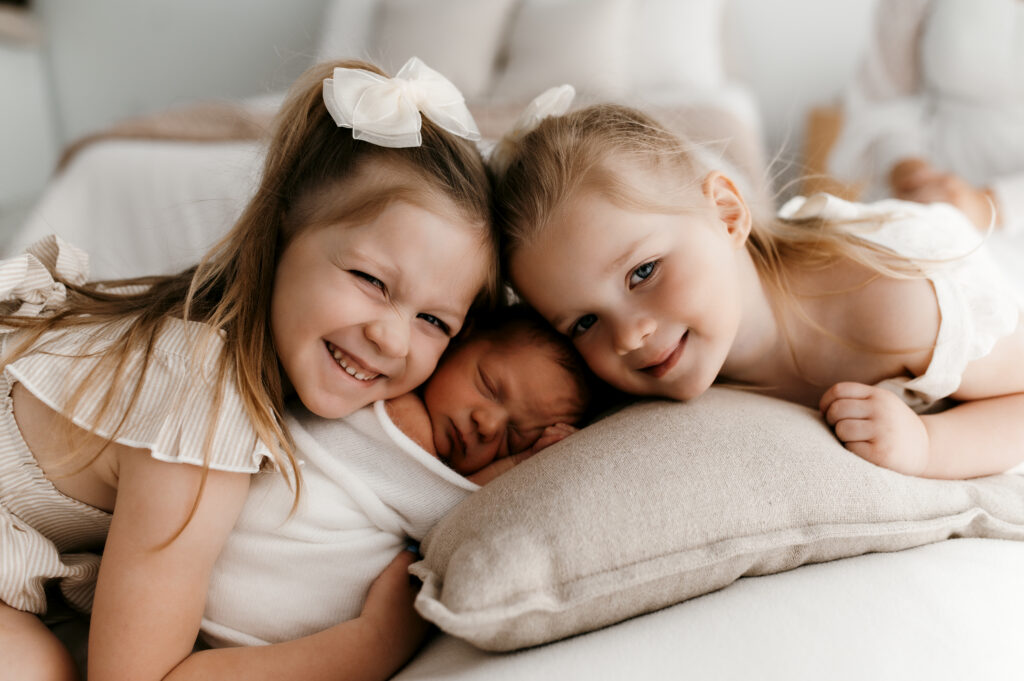 Sisters smiling with their new baby brother. 