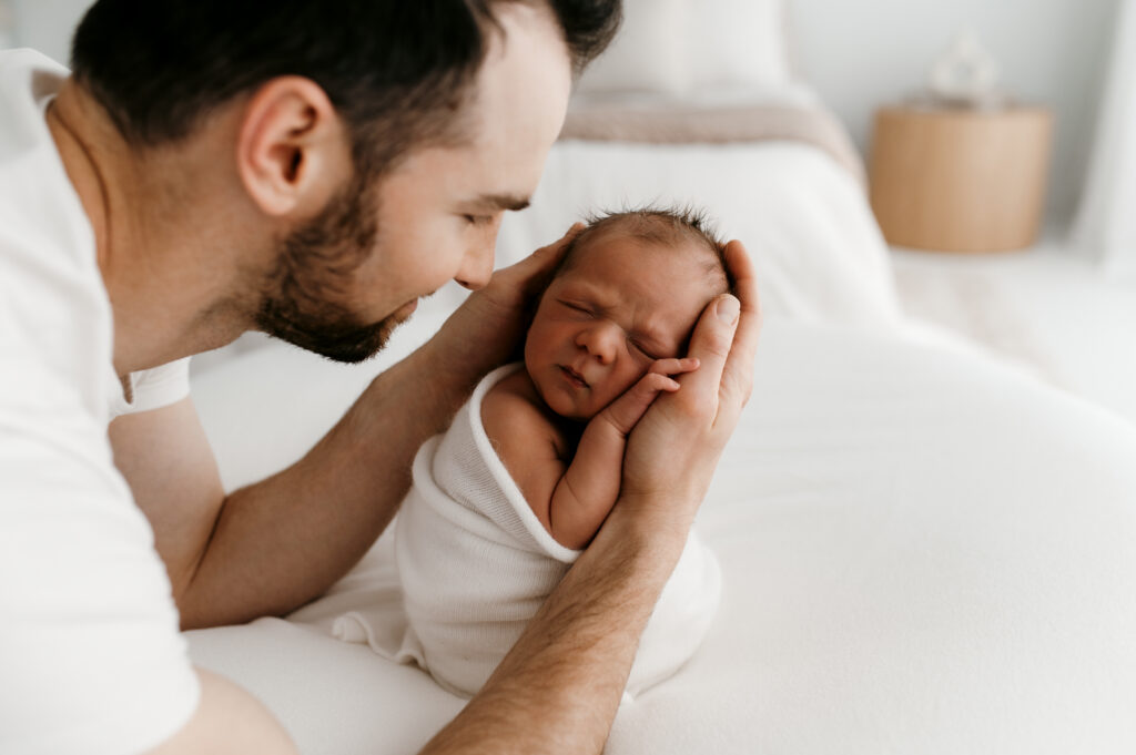 Dad holding newborn in neutral cream outfit during in-home lifestyle newborn session