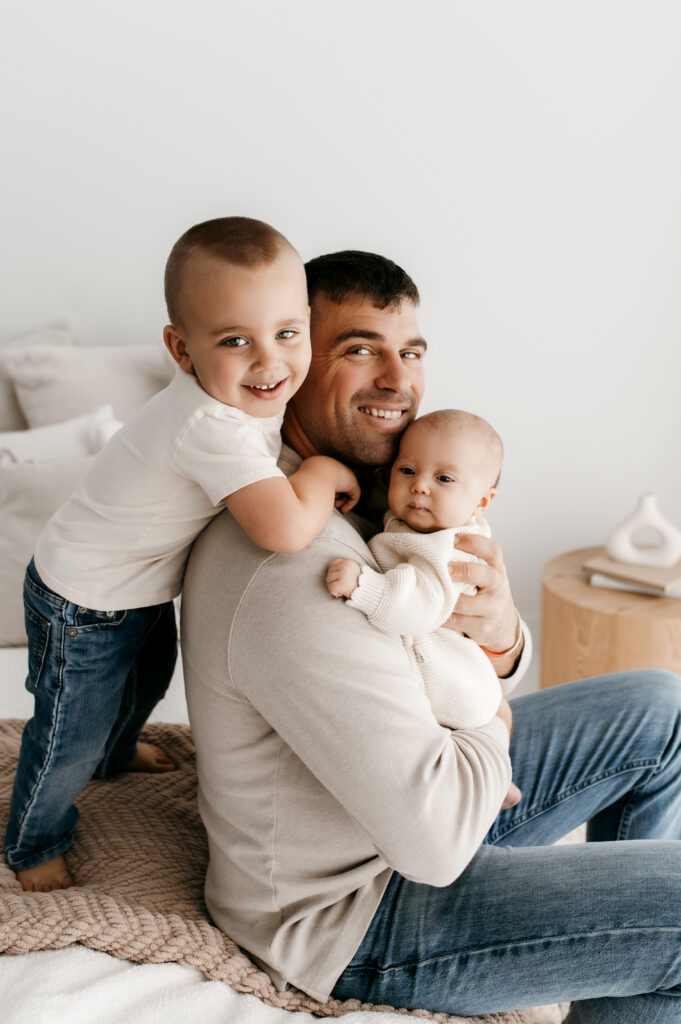 Dad and big brother snuggle newborn on a bed.