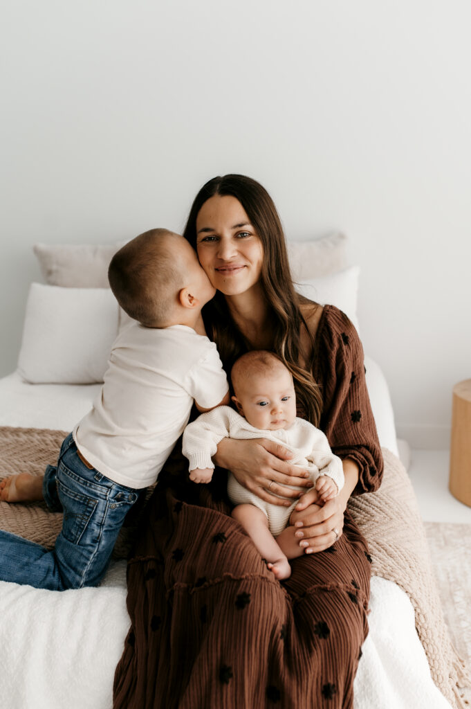Mom with big brother and newborn on the bed in natural light. 
