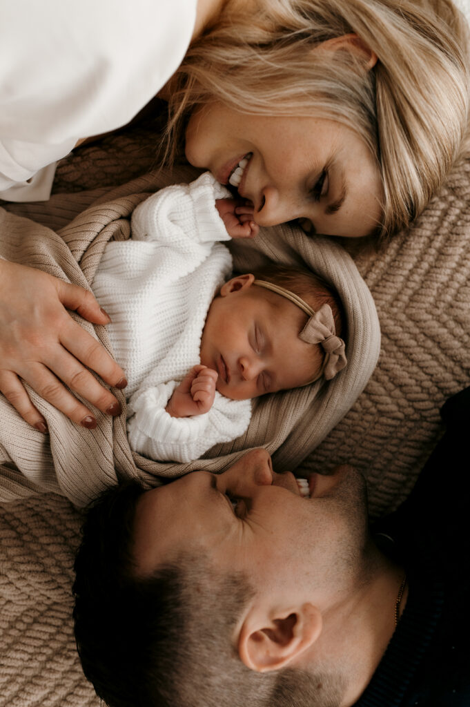 Parents snuggled next to newborn on a textured blankets. 