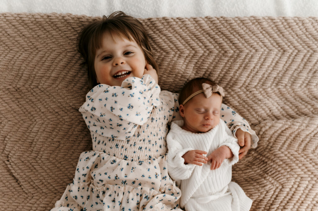 Big sister snuggling newborn on textured blankets for lifestyle photos.