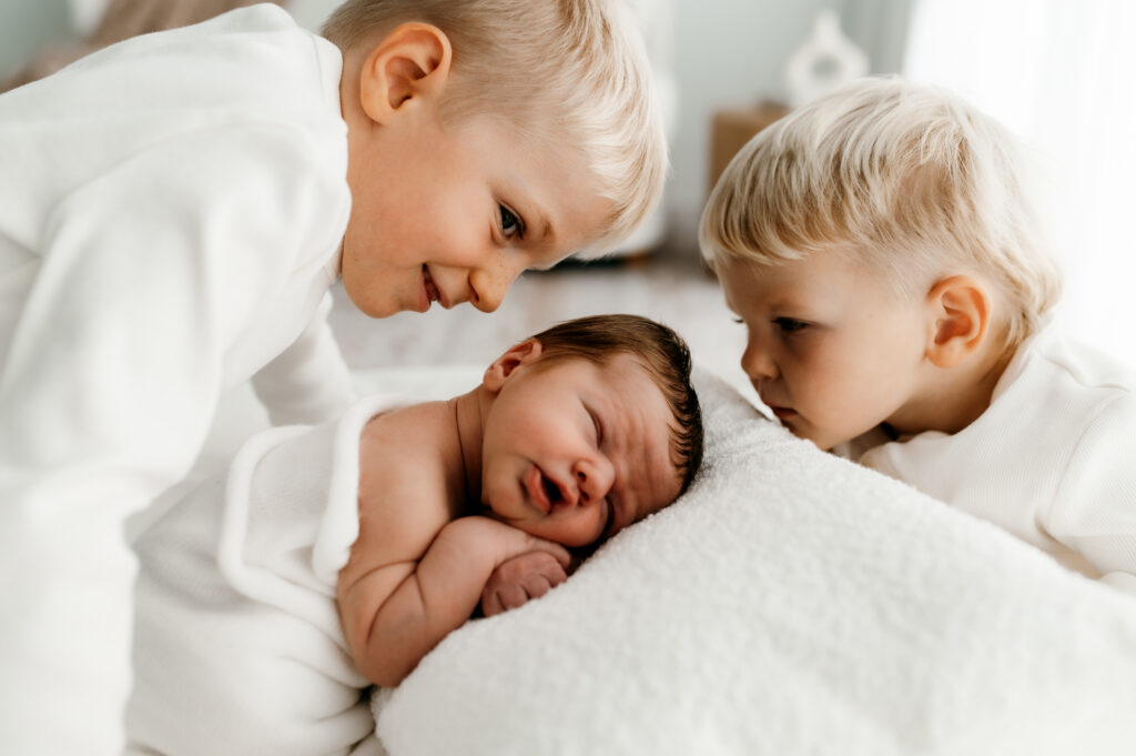candid moment of siblings interacting with newborn baby