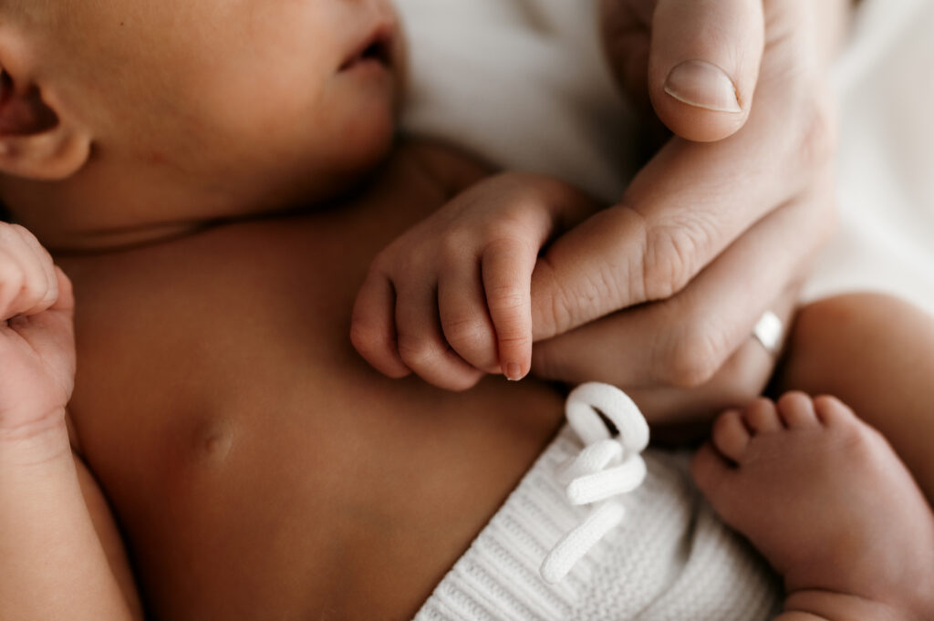 Close up of newborn fingers wrapped around parent’s thumb