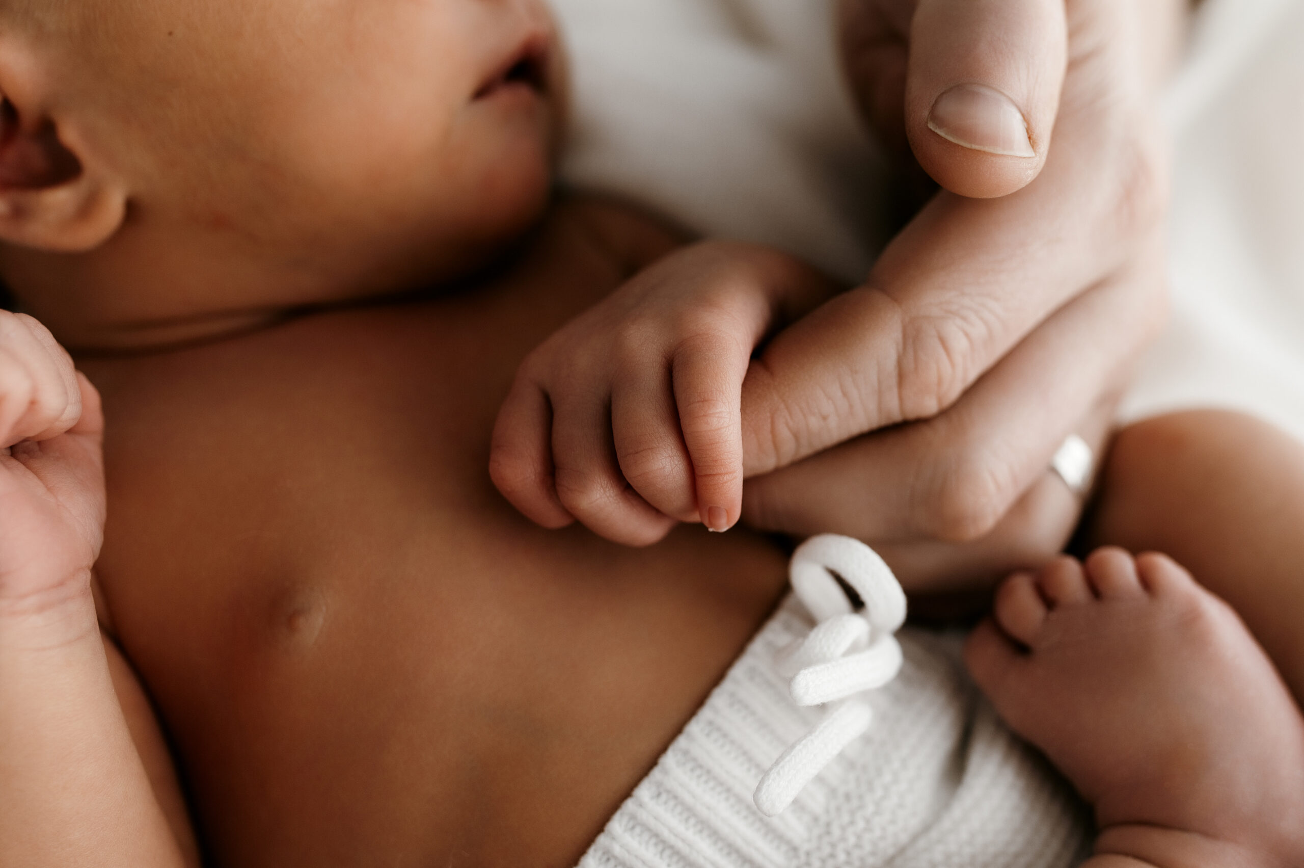 Close up of newborn fingers wrapped around parent’s thumb