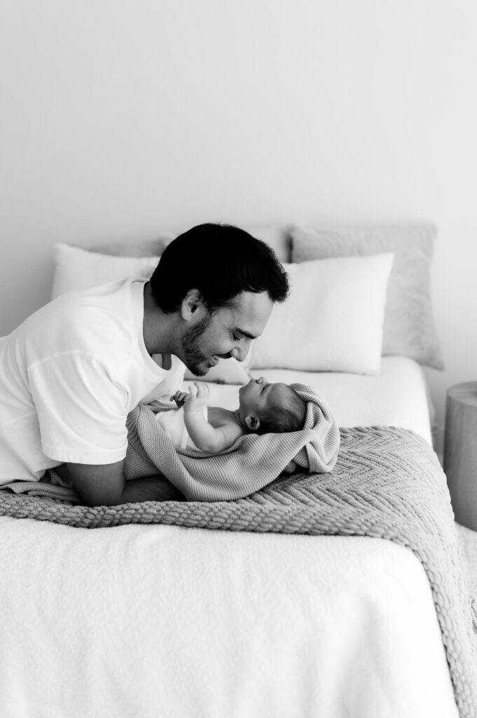 Father snuggling newborn on bed in soft natural window light