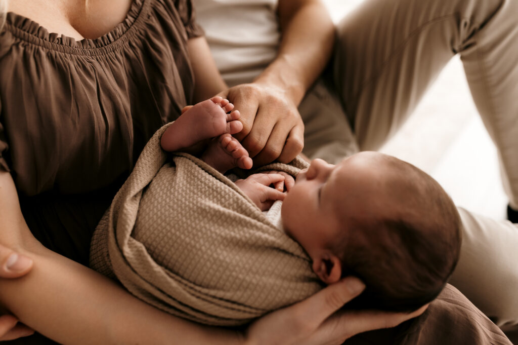 Mom seated on bed holding newborn securely with natural light