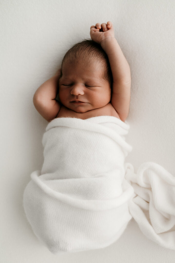Newborn with his arms stretched out in natural light