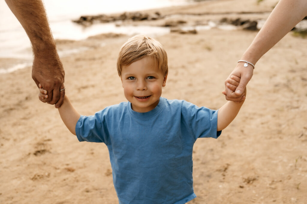 Little boys smiling while holding mom and dad's hands.